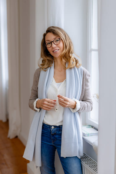 Mirja Schäffler-Hentschel Berufscoaching – stehend am großen hellen Fenster mit weißen Gardinen.