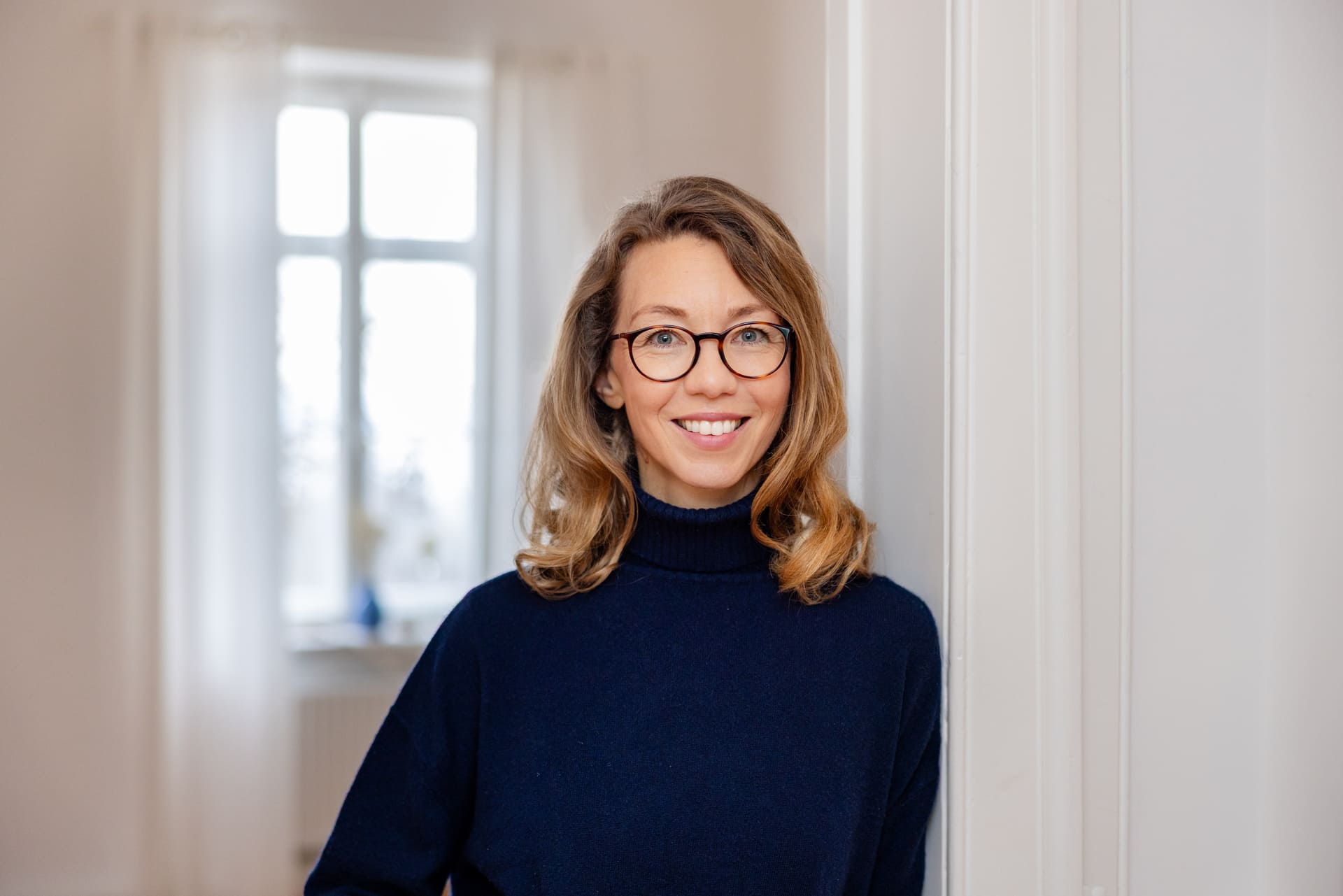 1. Mirja Schäffler-Hentschel Coaching in München – angelehnt am weißen Türrahmen in ihren Praxisräumen.