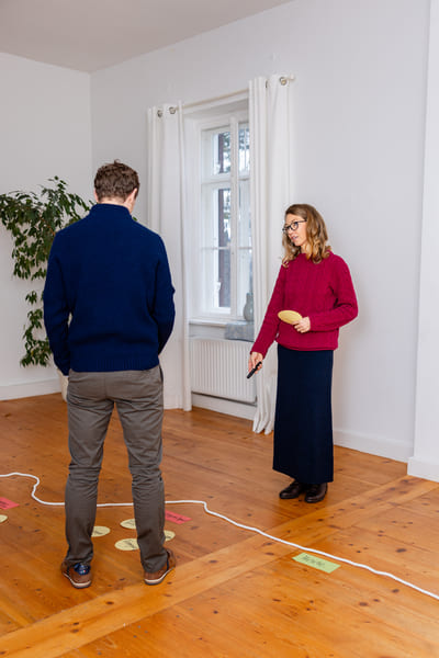 Mirja Schäffler-Hentschel Life Coaching in München – stehend und im Gespräch mit einem Coachee Arbeitsmaterialien auf dem Holzboden verteilt.